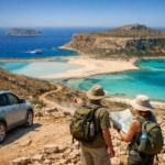 Travellers assess the rocky route to Balos Crete, overlooking turquoise lagoon, white sand, Gramvousa Peninsula, and a boat.